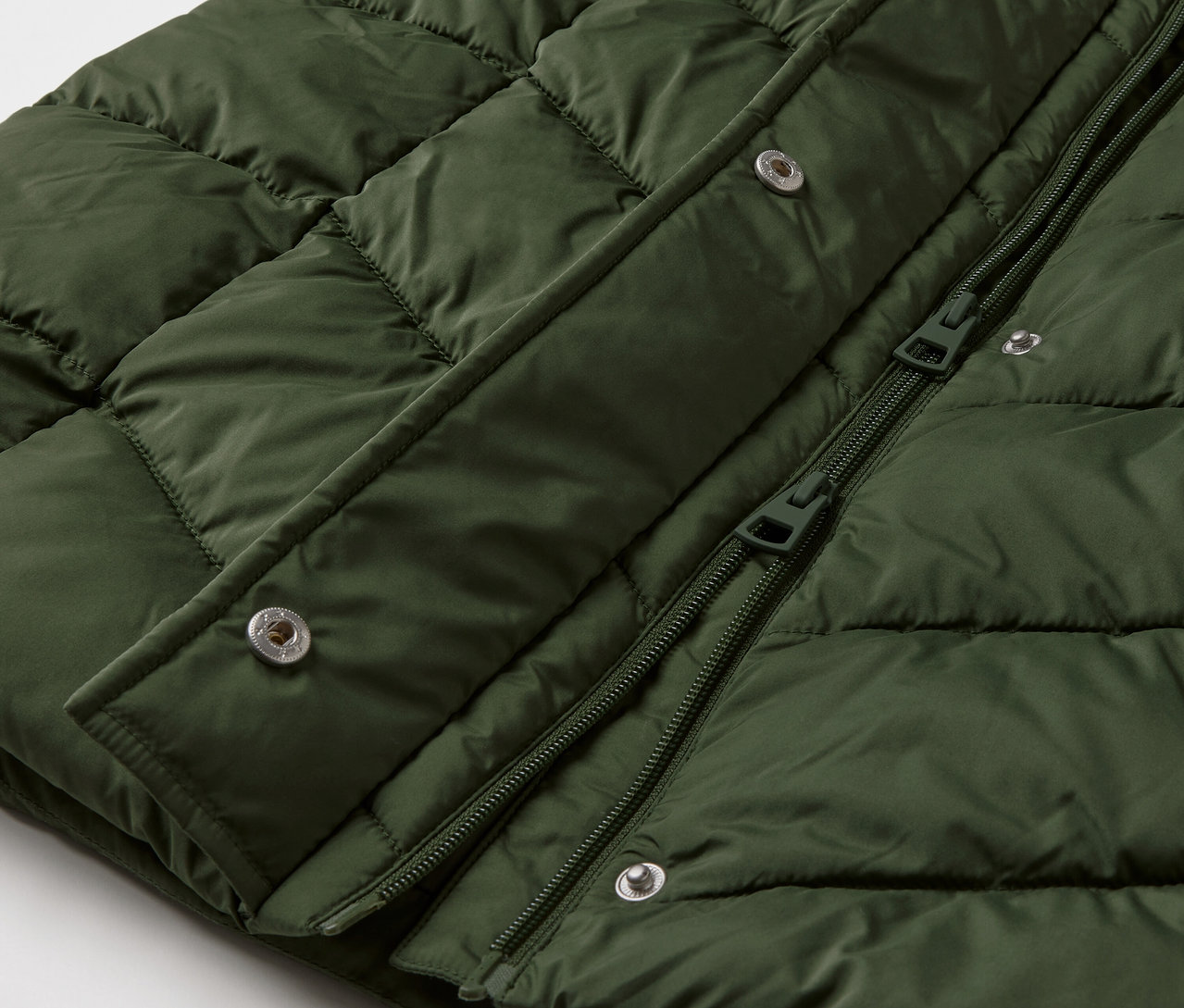 Gros plan sur un manteau matelassé à capuche vert foncé.
