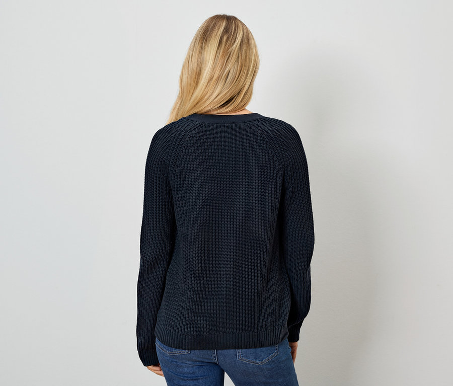 Une femme, vue de dos, porte un pull bleu marine et un jean.