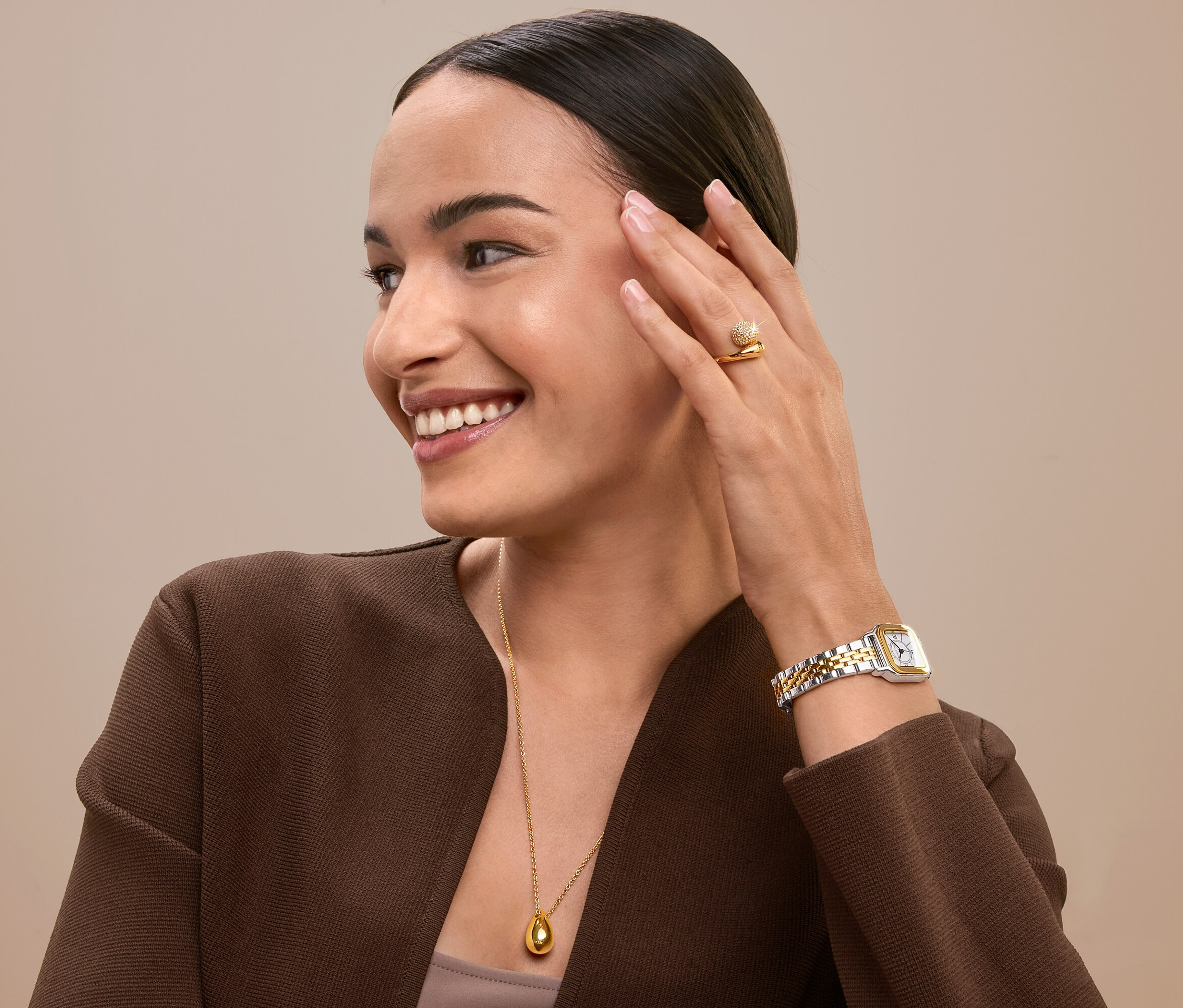 Femme souriante touchant son visage portant une bague, une montre et un collier en or.