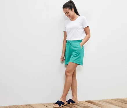 Femme debout, les mains dans les poches d'un short molletonné turquoise.