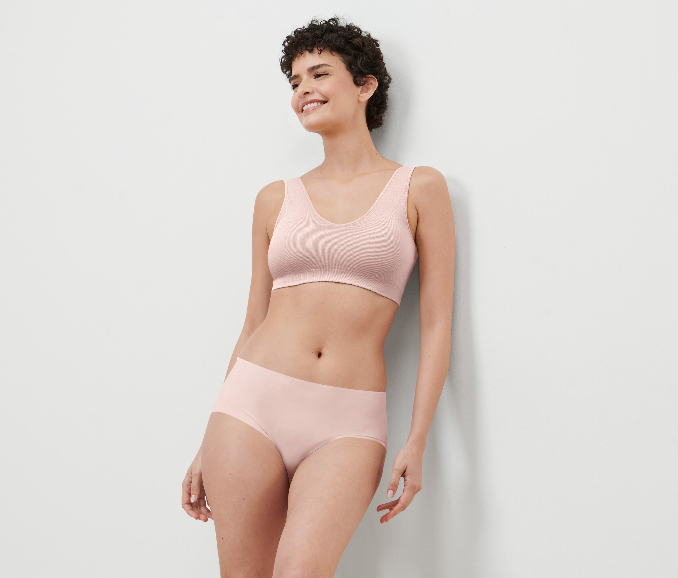 Une femme aux cheveux courts porte un soutien-gorge et une culotte roses.