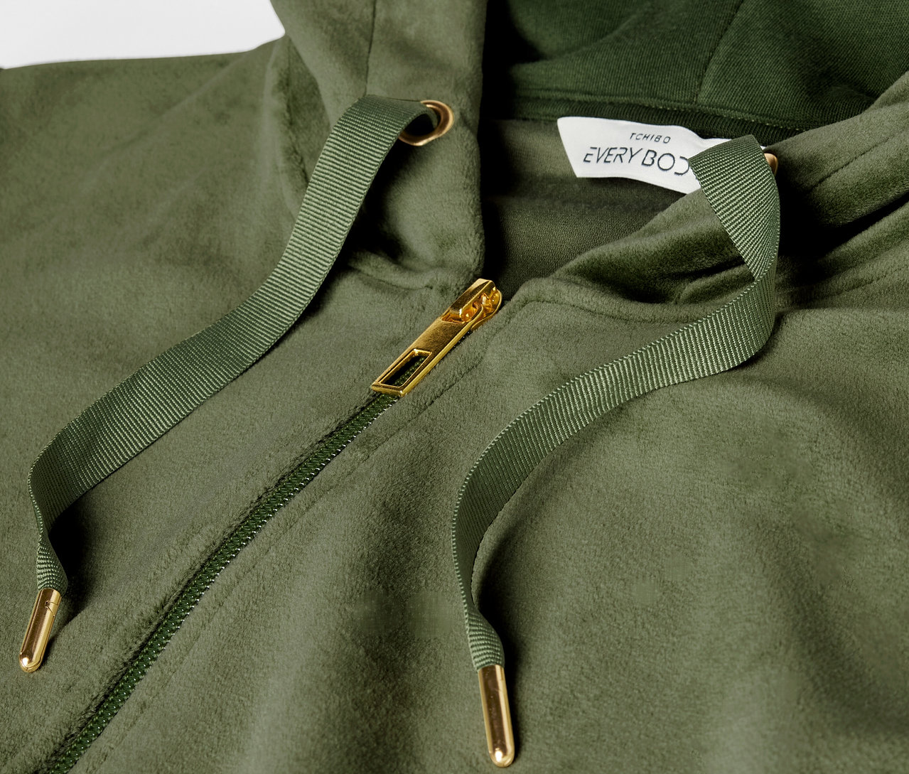 Gros plan sur un sweat à capuche vert avec fermeture éclair dorée et cordon de serrage.