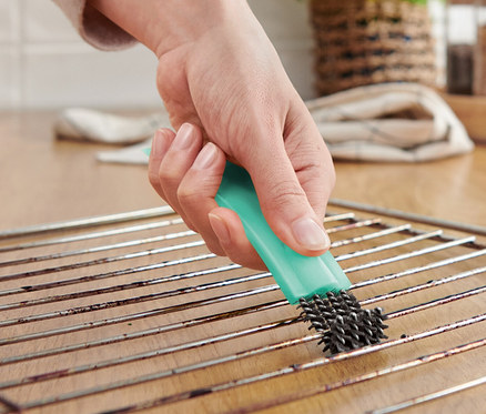Une personne nettoie une grille de four avec une brosse à four avec racloir.