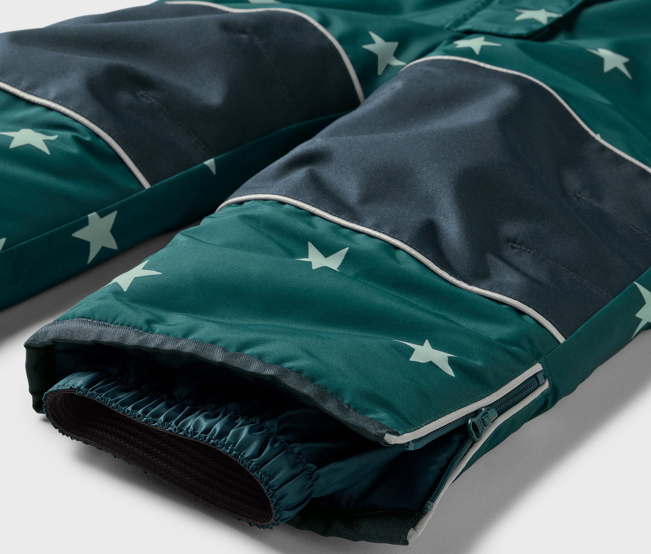 Détail d'un pantalon vert avec motif étoiles et genoux bleu foncé.