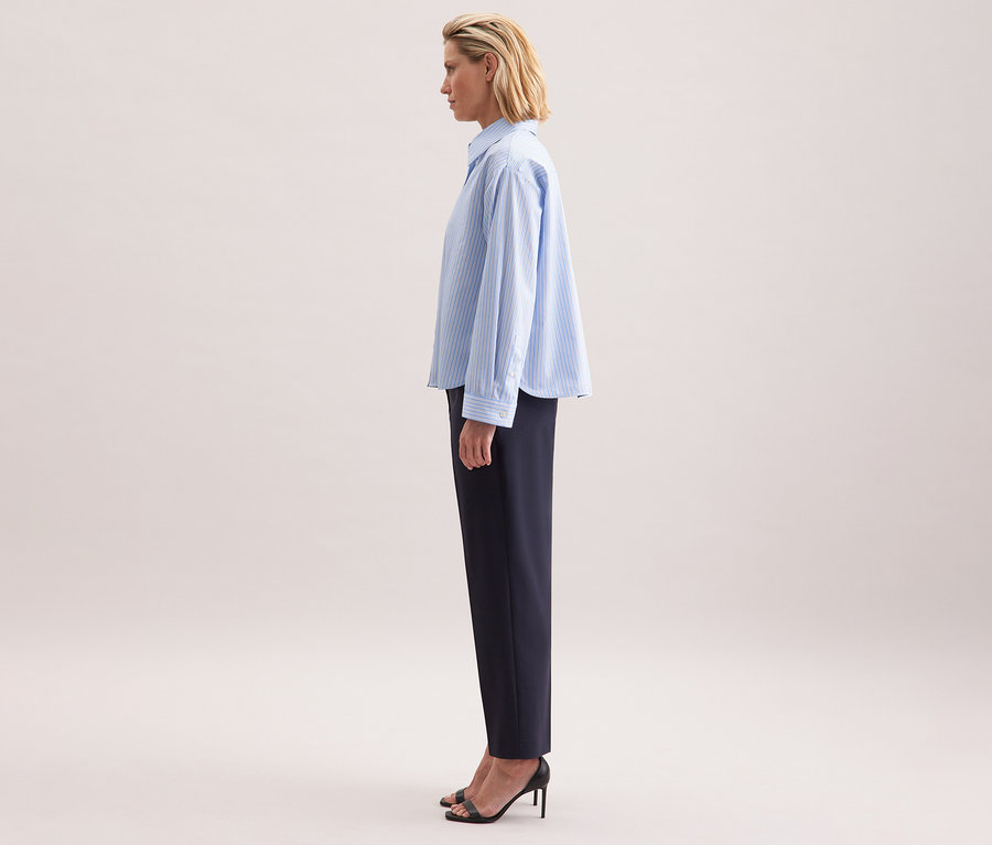 Femme de profil portant une chemise oversize Seidensticker et un pantalon foncé.