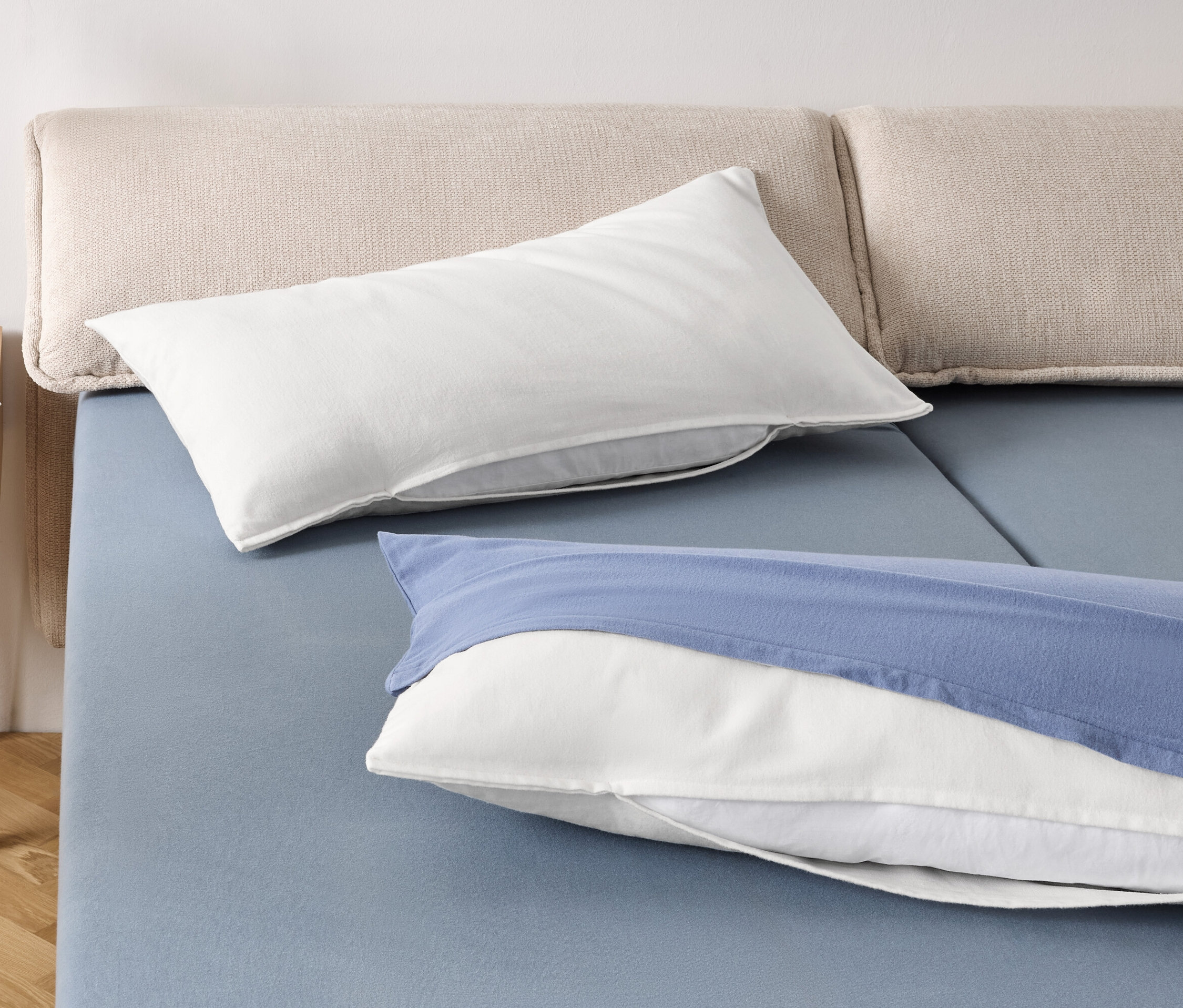 Deux oreillers blancs et un oreiller blanc avec une taie bleue sur un lit bleu.