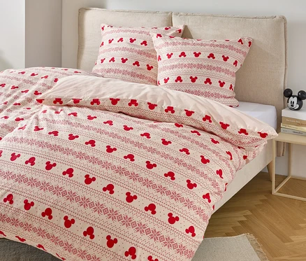 Lit avec des draps à motif Mickey Mouse et deux oreillers avec un motif similaire.