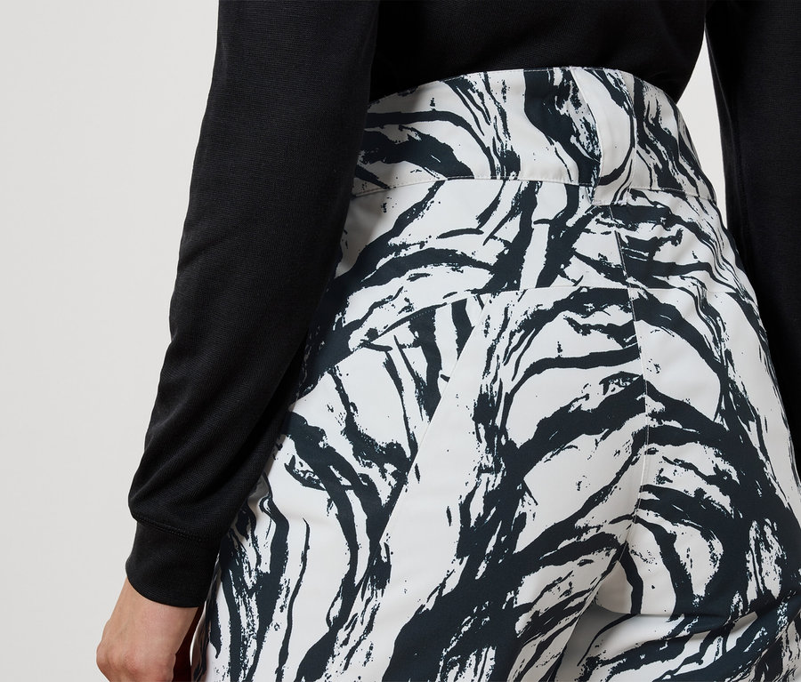 Vue arrière d'une femme portant un haut noir et un pantalon blanc avec un motif de branches noires.