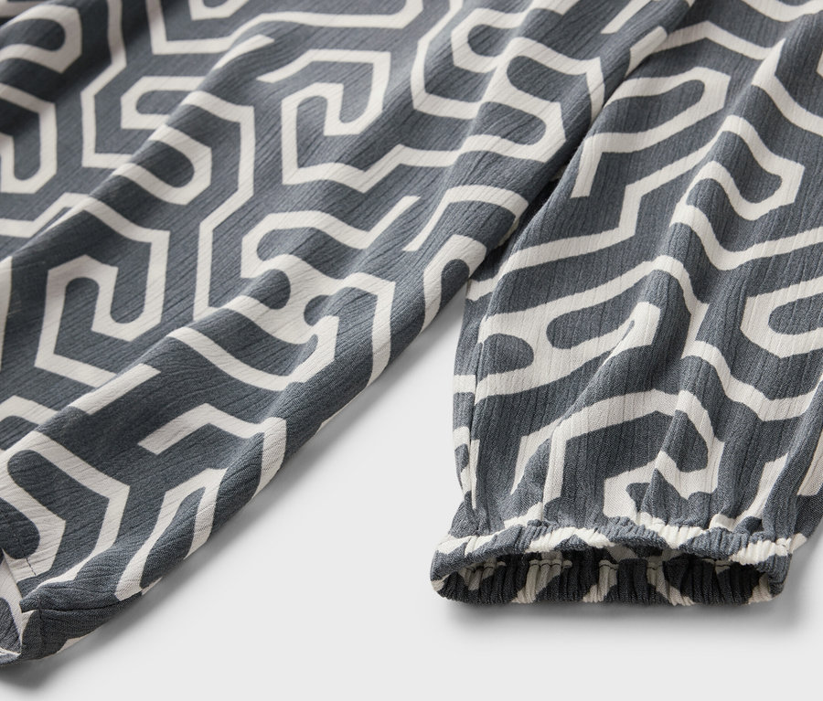 Détail d'une blouse grise aspect froissé avec un motif géométrique blanc.