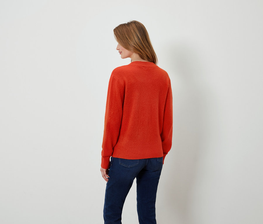 Femme portant un pull orange et un jean bleu foncé, dos à la caméra.