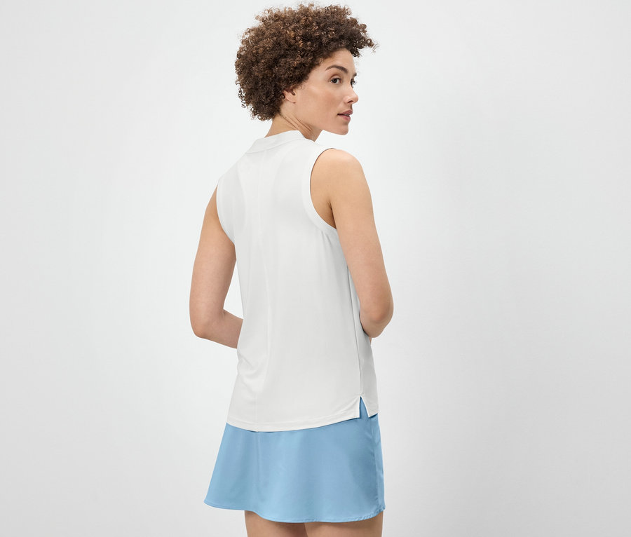 Femme portant un top fonctionnel blanc et une jupe bleue regardant par-dessus son épaule.