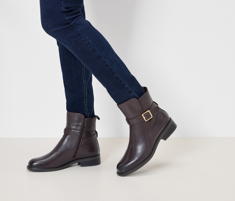 Jambes en jeans bleu foncé et bottines en cuir marron avec boucle et fermoir doré.