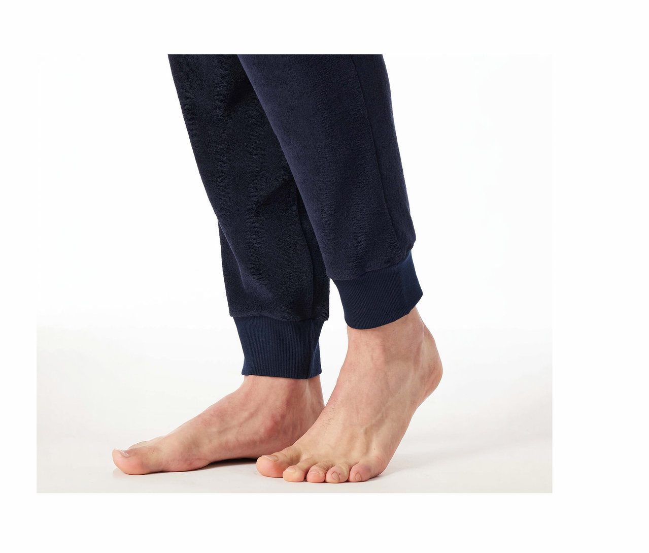 Pieds nus et bas de jambes d'une personne portant un pantalon de pyjama en tissu éponge SCHIESSER bleu foncé avec des poignets côtelés sur fond blanc.