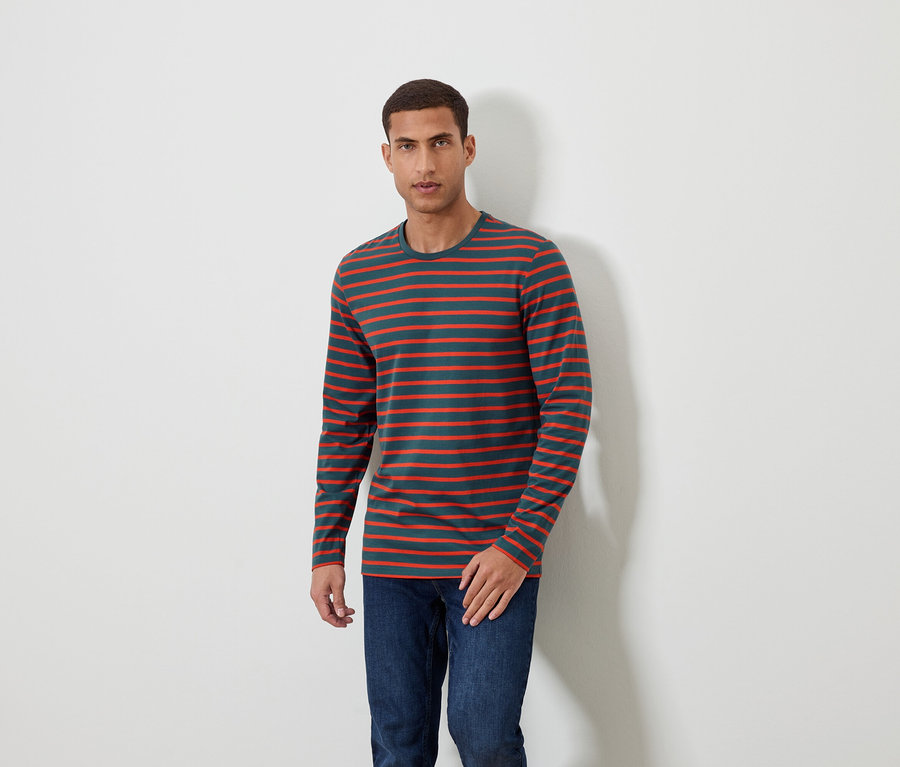 Un homme debout portant un t-shirt rayé à manches longues et un jean.