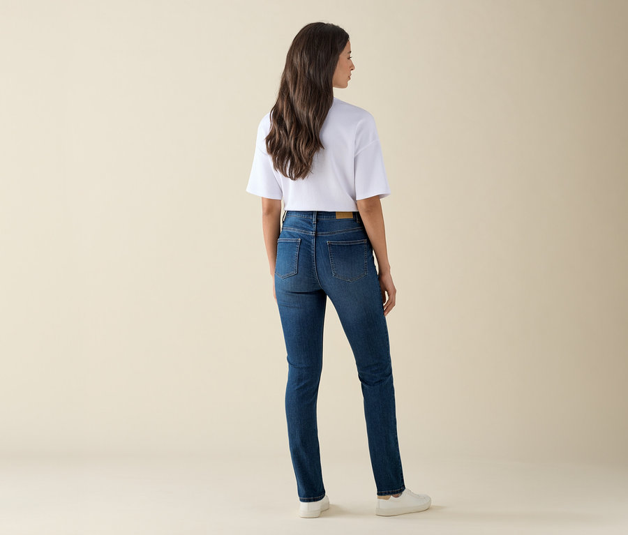 Une femme se tient dos à la caméra et porte un jean slim – Coupe « Emma », denim bleu moyen, un t-shirt blanc et des baskets.