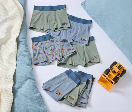 Sur un lit, plusieurs boxers pour garçons avec des motifs de voitures et un bulldozer jouet jaune.