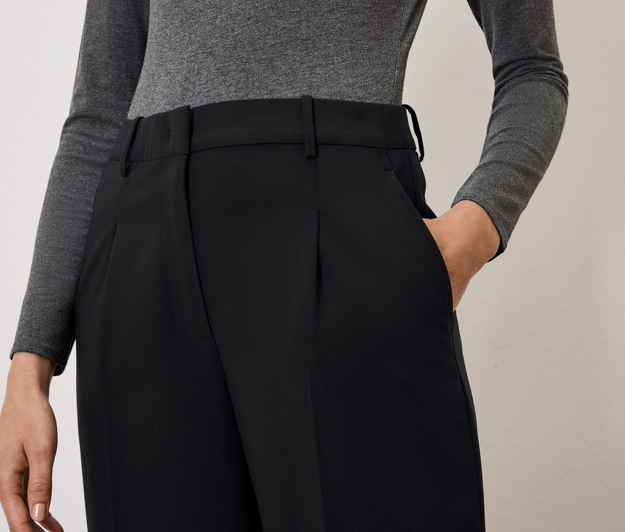 Une femme a la main dans la poche d'un pantalon noir.