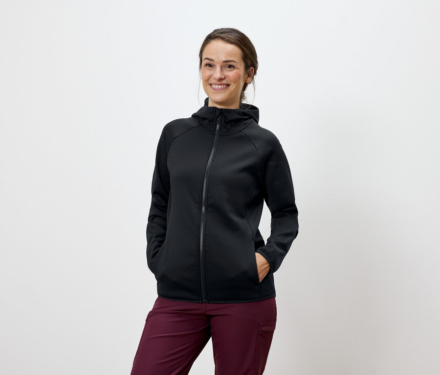 Une femme pose en sweat à capuche noir et pantalon bordeaux.