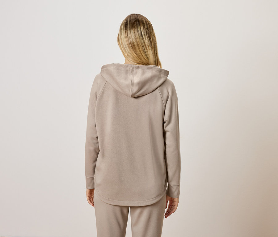 Une femme portant un sweat à capuche beige et un pantalon de survêtement, vue de dos.