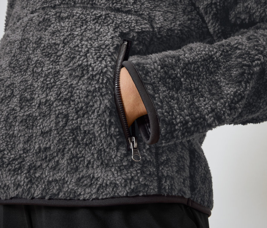 Gros plan sur une veste en polaire grise avec une main dans la poche.