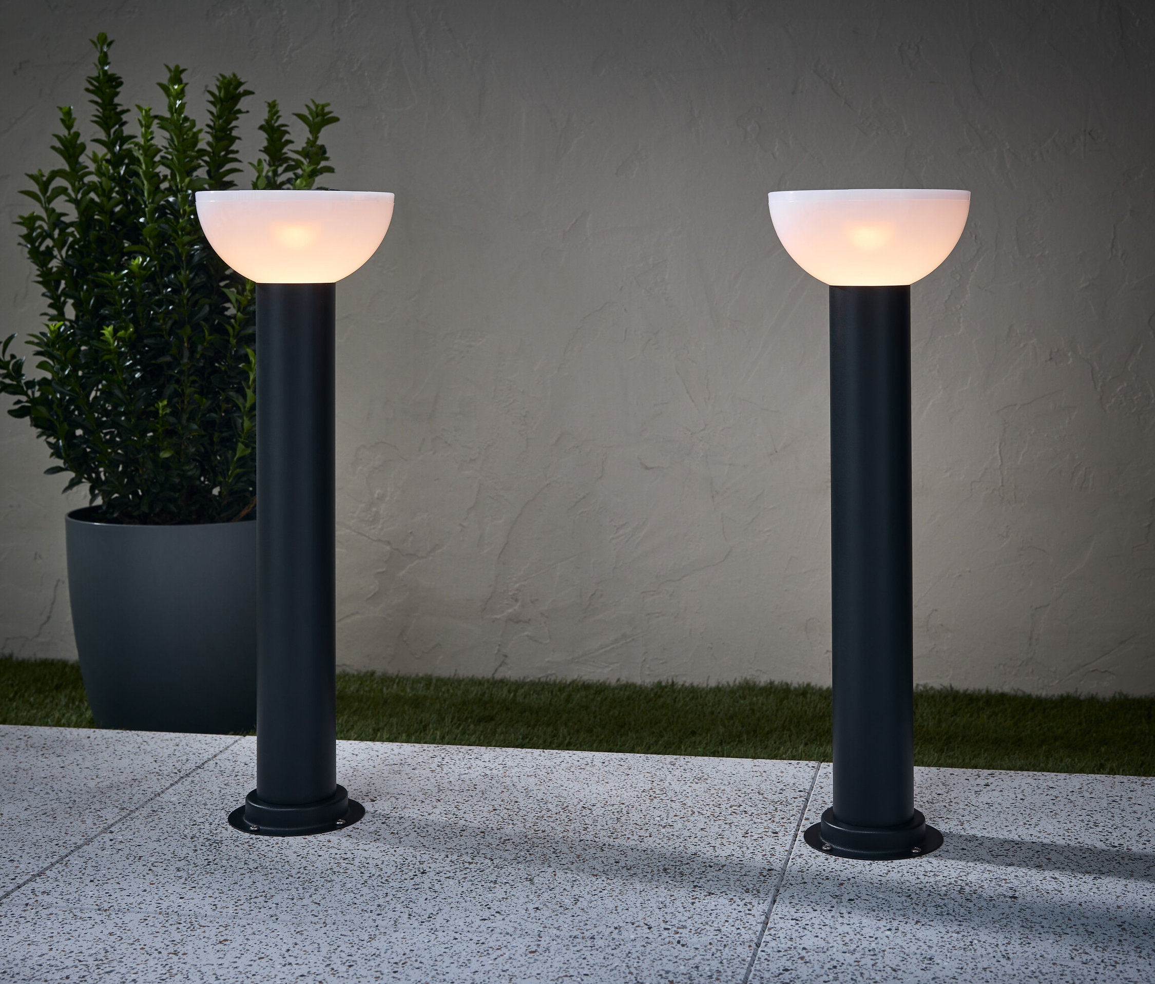 Deux lampes solaires directionnelles éclairent un chemin. Un pot de fleurs est placé à côté d'une lampe.