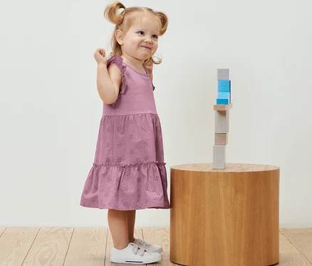 Petite fille souriante en robe pour enfant debout à côté de blocs de bois sur une table ronde.