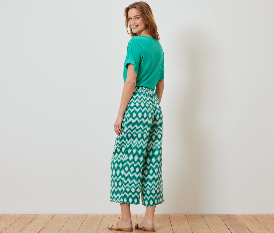 Une femme pose dans un t-shirt vert et un pantalon en satin imprimé.