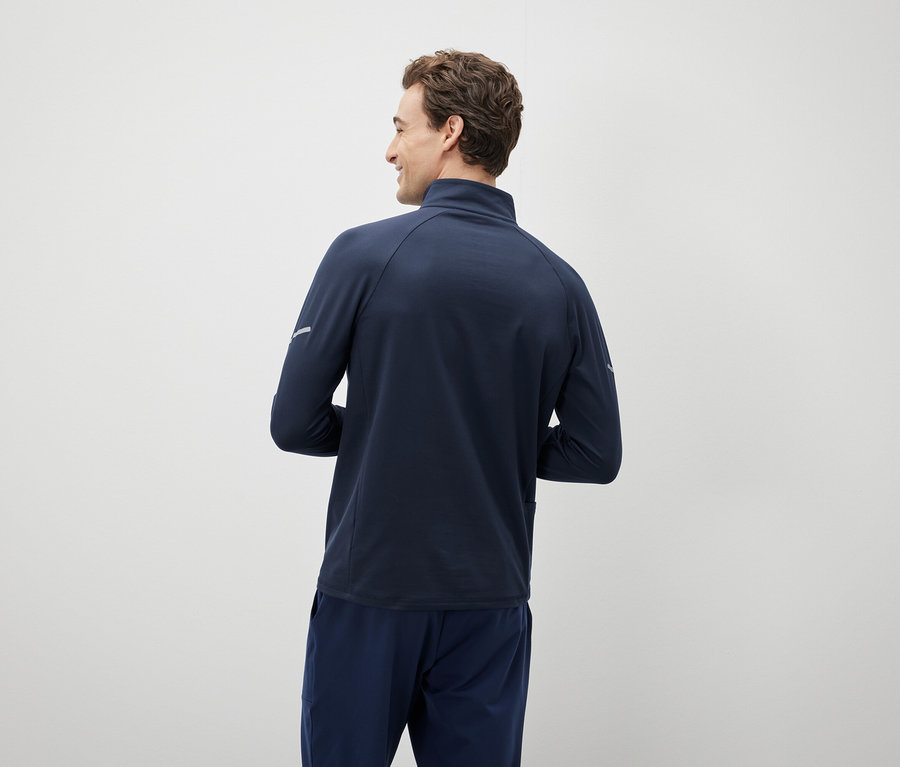 Un homme regarde par-dessus son épaule et porte une veste et un pantalon bleu marine.