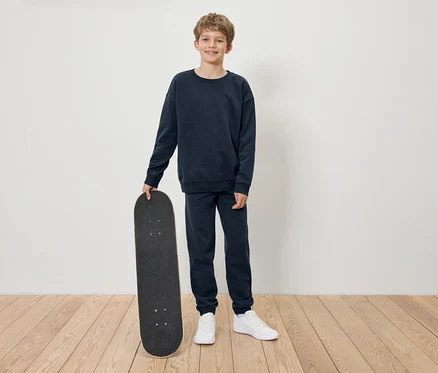Garçon en survêtement bleu marine tenant un skateboard.