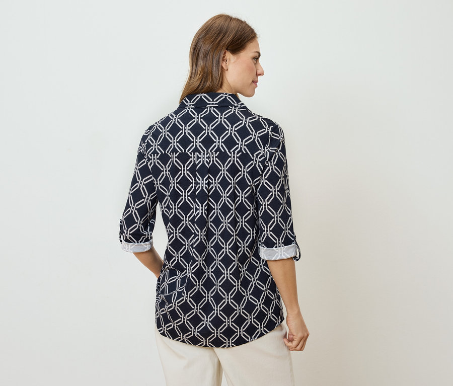 Vue arrière d'une femme aux cheveux bruns portant un chemisier bleu marine à manches longues avec un motif géométrique blanc et un pantalon beige.