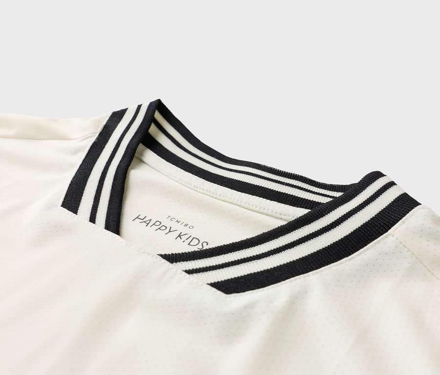 Vue détaillée d'un t-shirt blanc avec un col rayé noir et blanc et le logo 'TCHIBO HAPPY KIDS'.