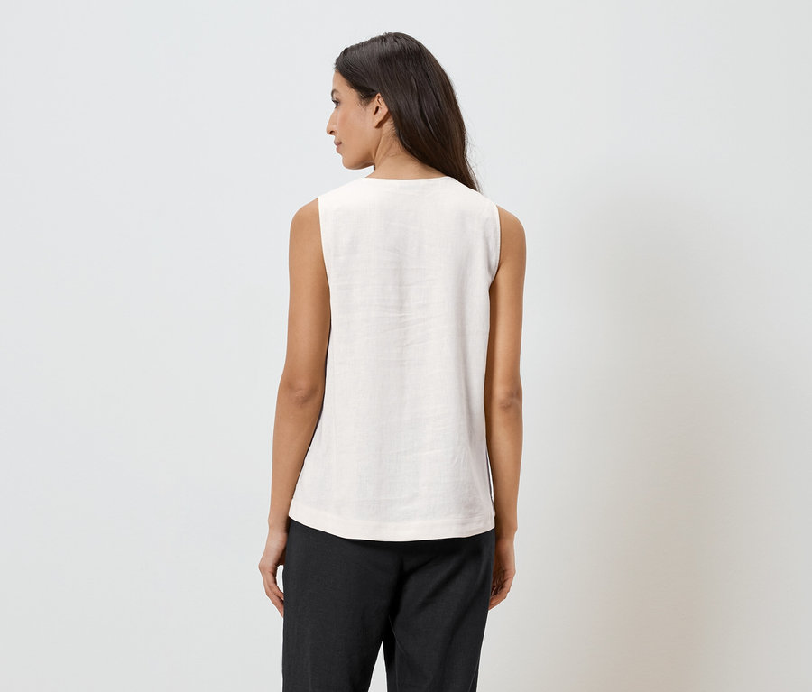 Femme vue de dos, portant un haut clair et un pantalon foncé sur un fond clair.