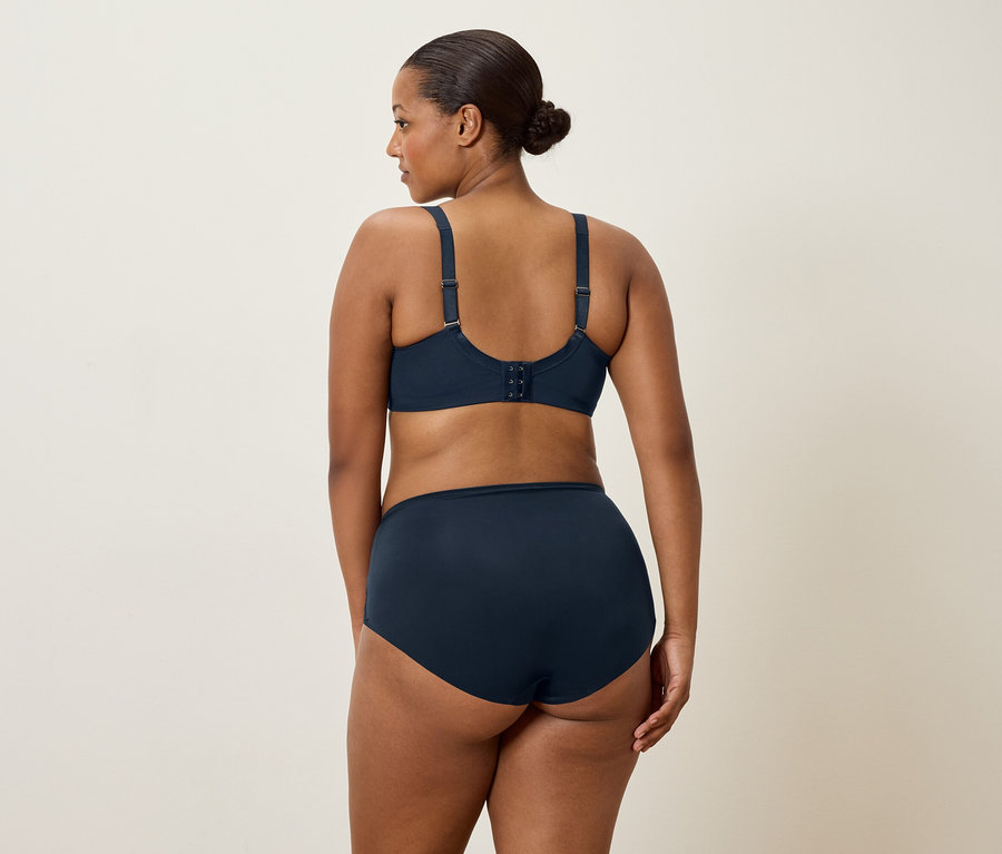 Une femme aux cheveux foncés, vue de dos, porte un soutien-gorge bleu marine et une culotte assortie.