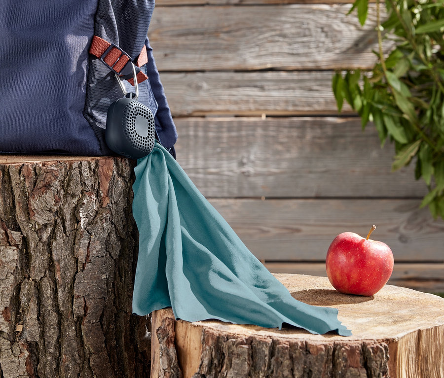 Sac à dos bleu avec un haut-parleur attaché à un mousqueton et un tissu turquoise sur une souche d'arbre, à côté d'une pomme rouge.