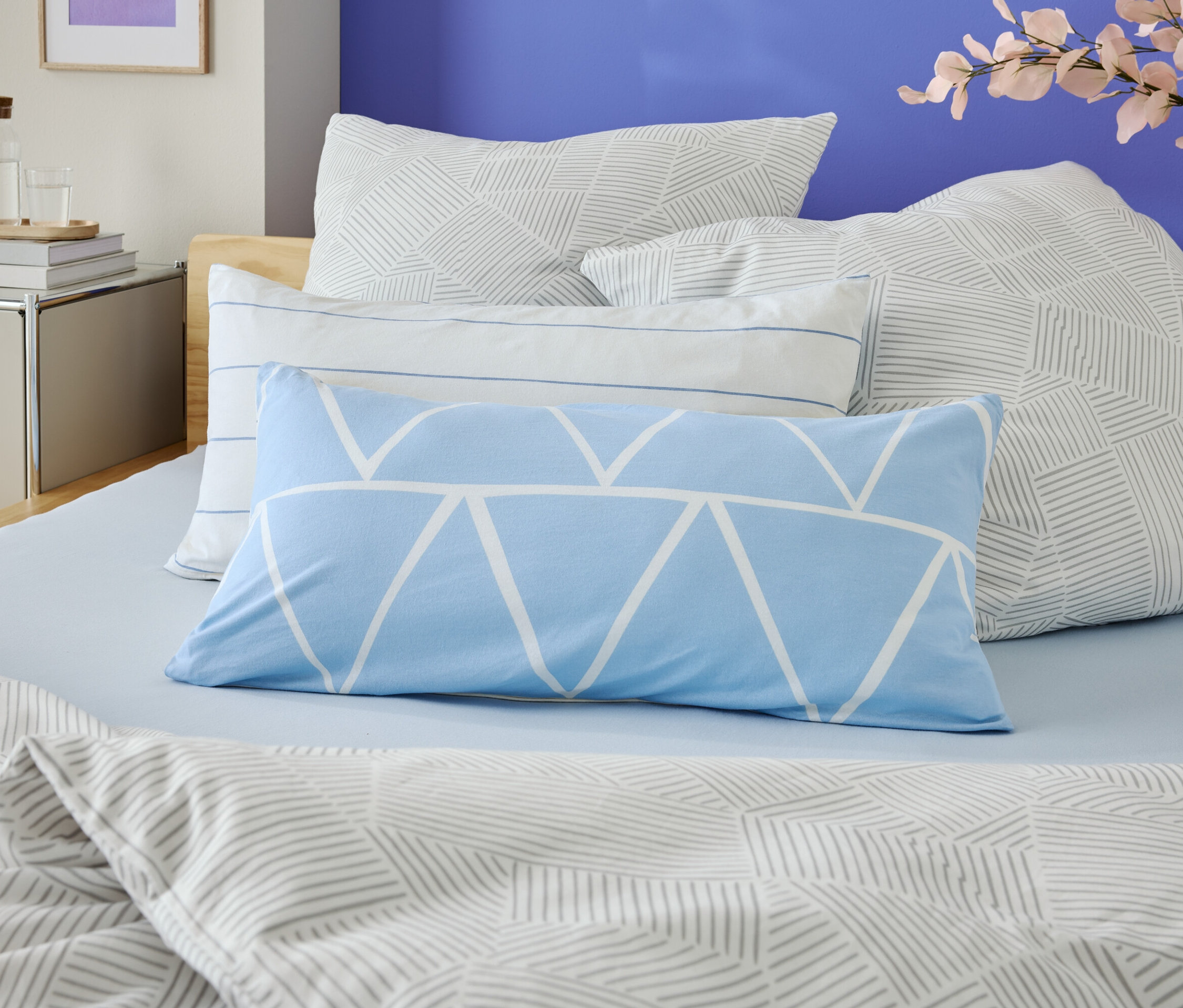 Gros plan d'un lit avec des draps bleu clair et plusieurs coussins à motifs géométriques.