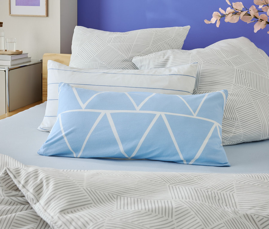 Gros plan d'un lit avec des draps bleu clair et plusieurs coussins à motifs géométriques.