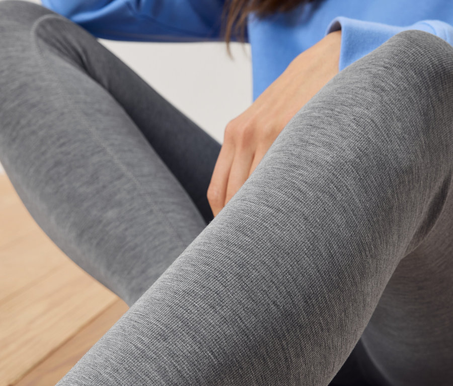 Gros plan d'une femme portant des leggings gris et un pull bleu, assise sur un plancher en bois.