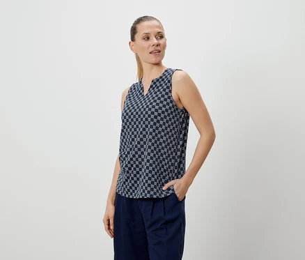 Femme portant un chemisier à motifs bleus et un pantalon bleu, une main dans la poche.