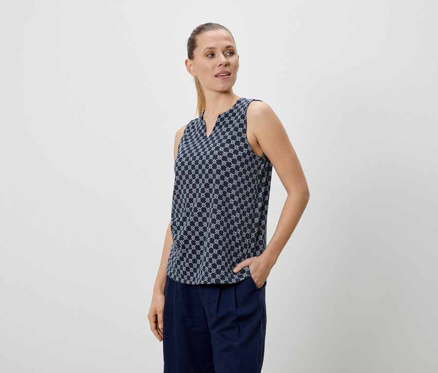 Femme portant un chemisier à motifs bleus et un pantalon bleu, une main dans la poche.