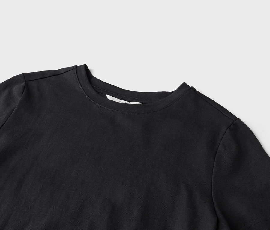 Gros plan d'un t-shirt noir à col rond sur un fond gris clair.