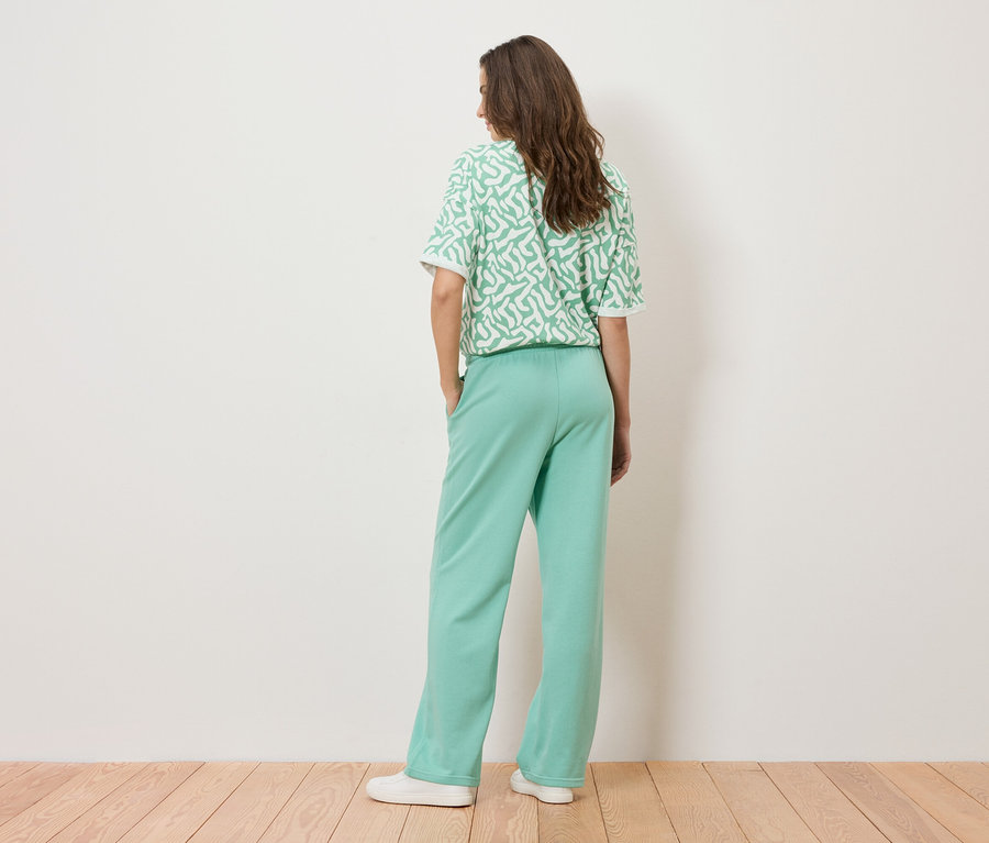 Une femme se tient dos à la caméra, elle porte une tenue vert menthe composée d'un pantalon et d'un t-shirt à motifs blancs.