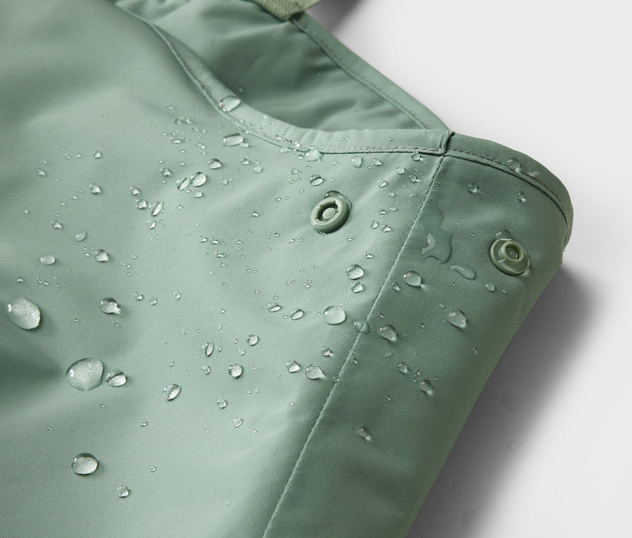 Gros plan d'un tissu vert menthe imperméable avec des boutons-pression et des gouttes d'eau.