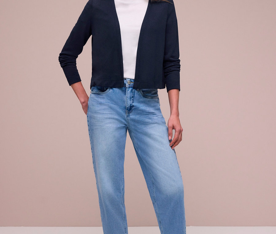 Femme debout, mains dans les poches, portant un cardigan Street One bleu foncé sur un t-shirt blanc, un jean bleu clair et des baskets argentées.