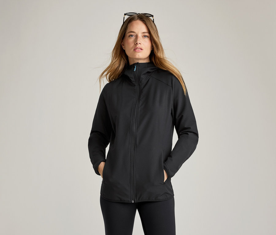 Une femme portant des lunettes de soleil sur la tête porte une veste noire en softshell.