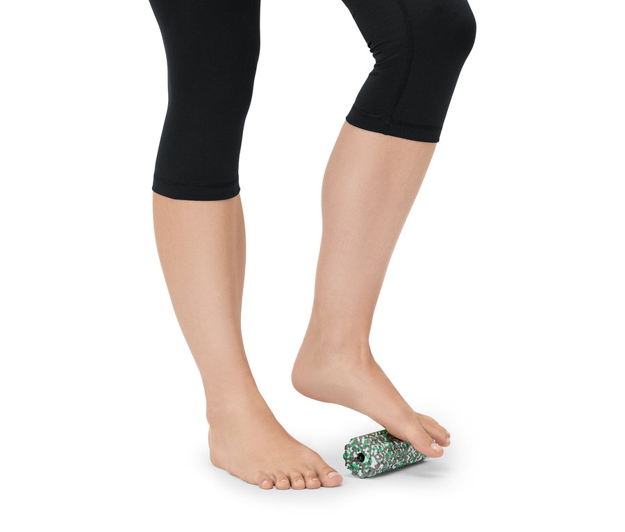 Femme en legging noir faisant rouler son pied sur un rouleau en mousse vert et blanc.