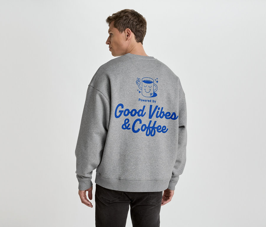 Homme de dos portant un pull gris avec un imprimé bleu 'Good Vibes & Coffee'.