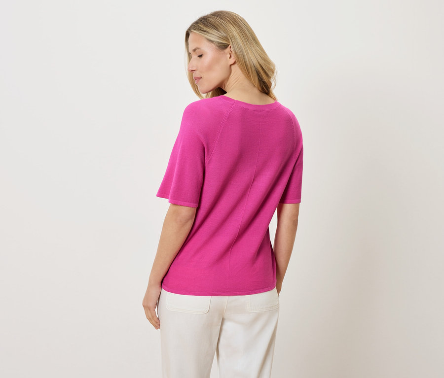 Vue arrière d'une femme blonde portant un t-shirt rose à manches courtes et un pantalon blanc.
