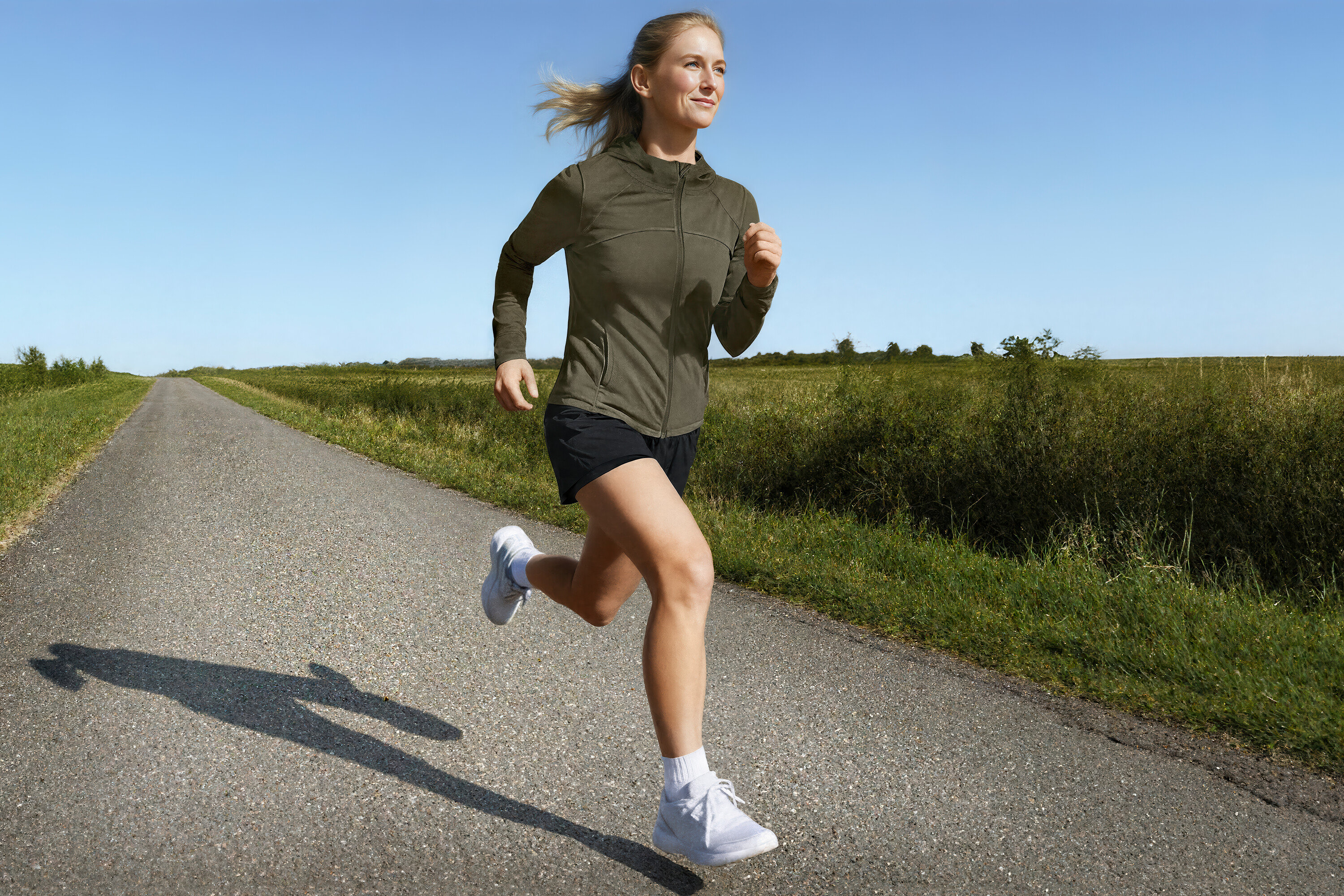 Femme courant sur une route de campagne en veste de sport et short de course 2 en 1.