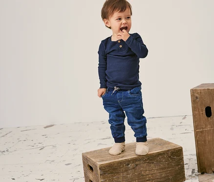 Un jeune enfant debout sur une caisse en bois porte un t-shirt côtelé à manches longues NAME IT bleu marine.