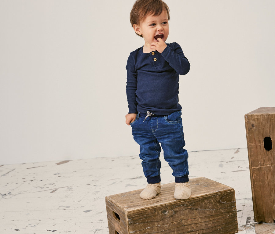 Un jeune enfant debout sur une caisse en bois porte un t-shirt côtelé à manches longues NAME IT bleu marine.